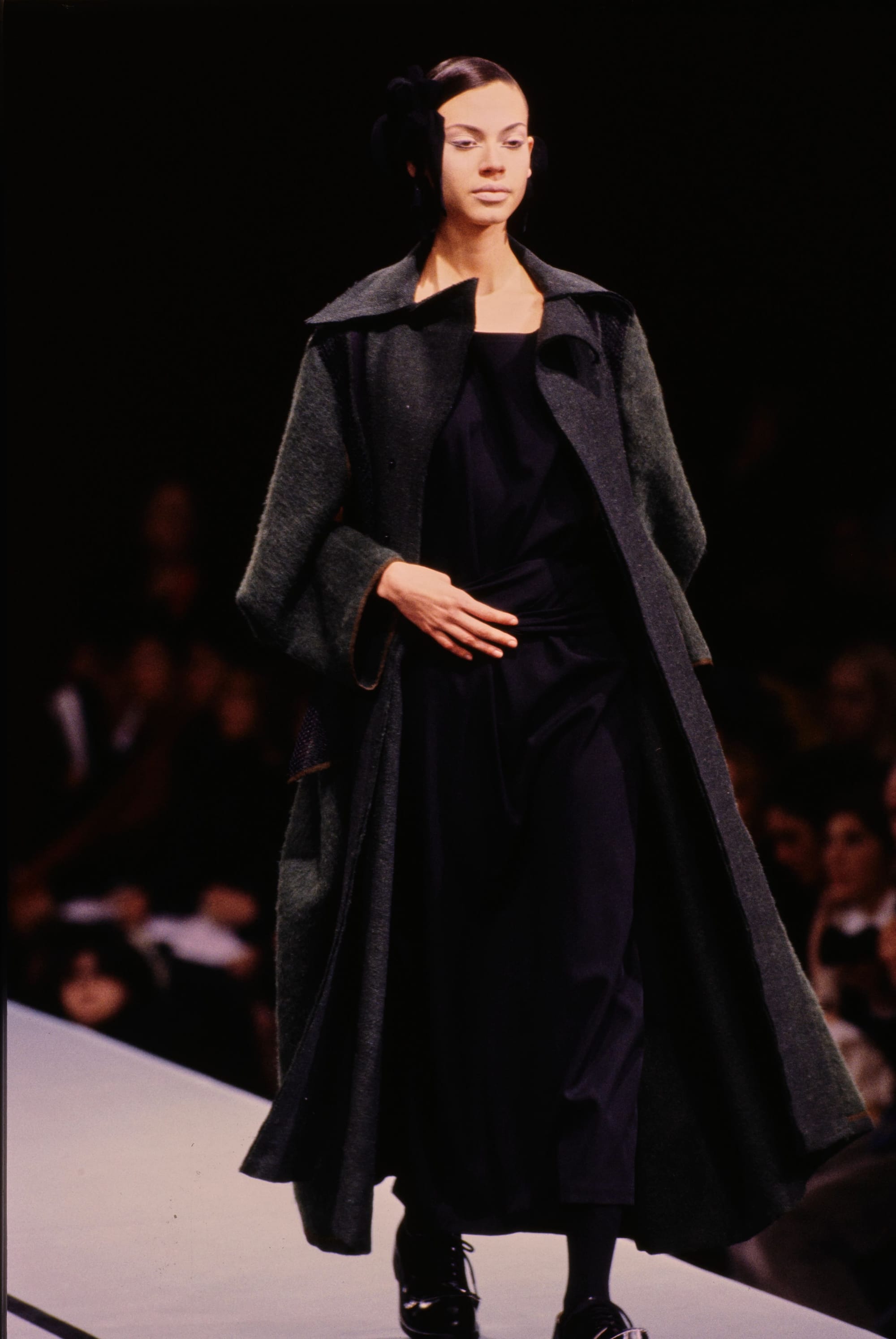 Yohji Yamamoto Fall 1995 detail 63: Long dark grey coat open over a black dress with fabric wrapped at the waist.