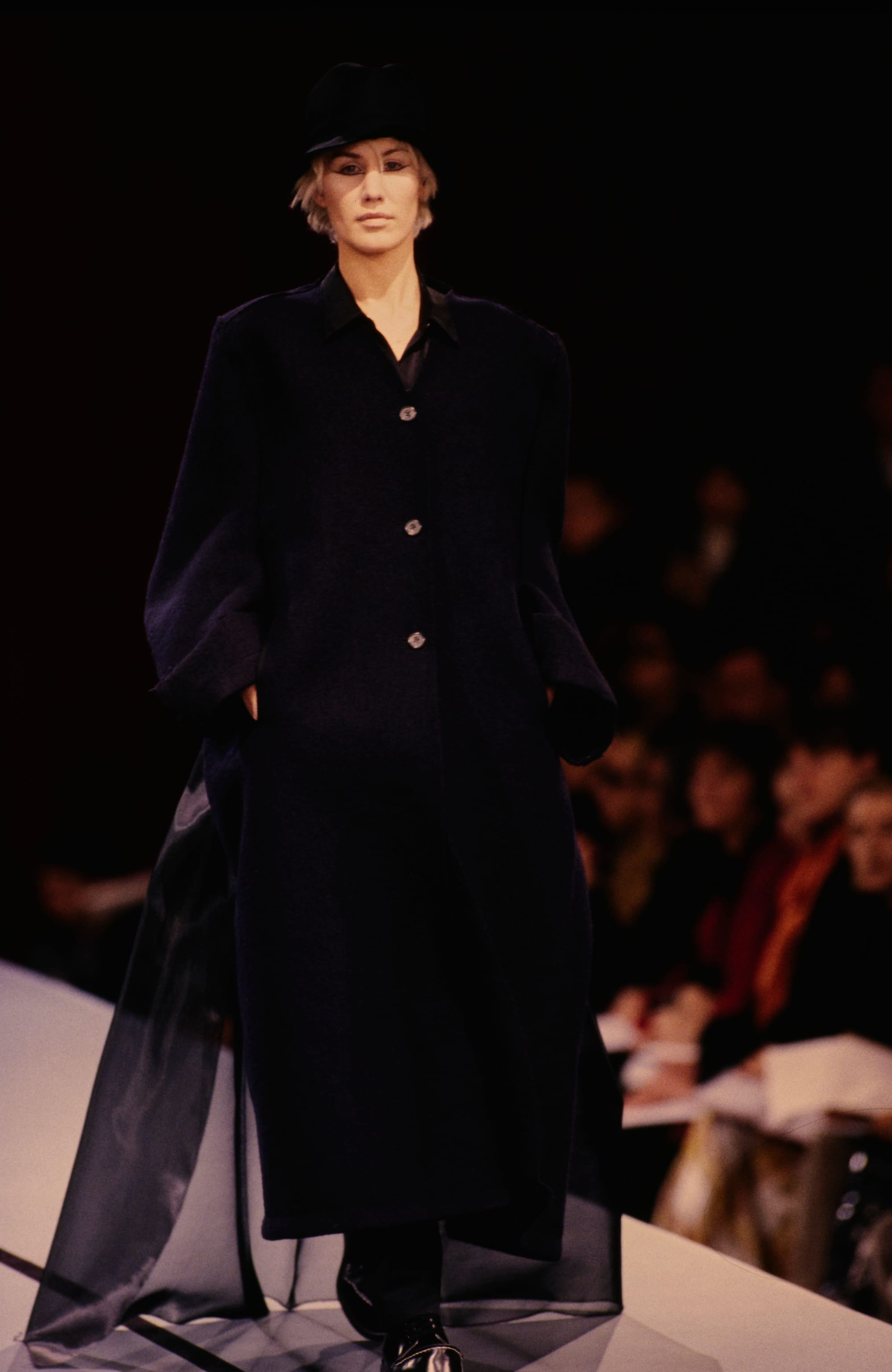 Yohji Yamamoto Fall 1995 detail 66: Long dark buttoned coat with sheer black panels trailing from both sides.