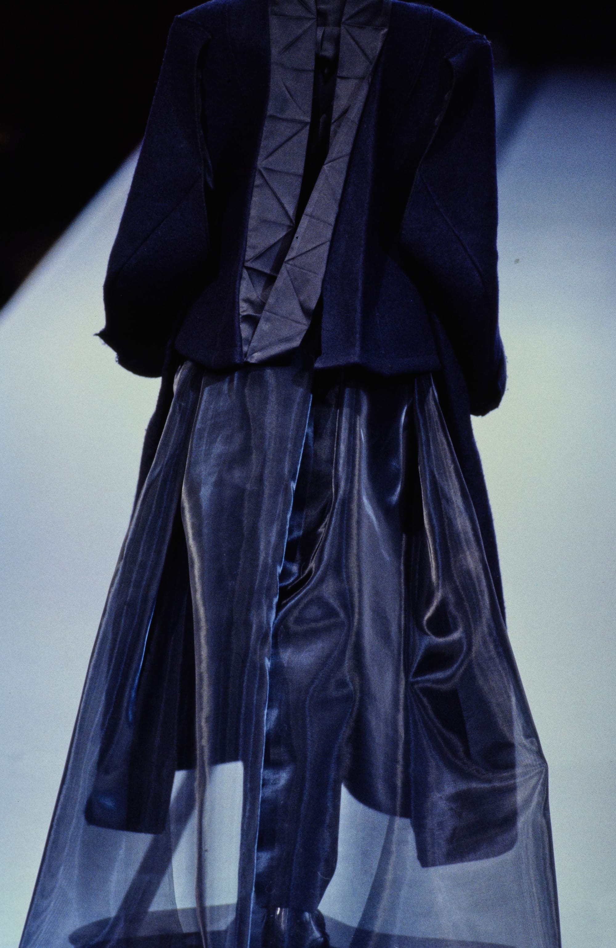 Yohji Yamamoto Fall 1995 detail 67: Rear dark jacket with a pleated geometric back above a translucent outer skirt.