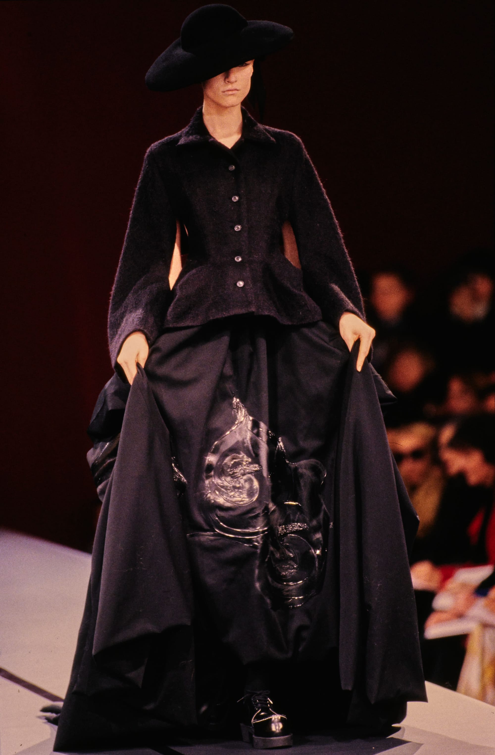 Yohji Yamamoto Fall 1995 detail 70: Broad black hat, fitted dark jacket and full skirt with glossy appliques.
