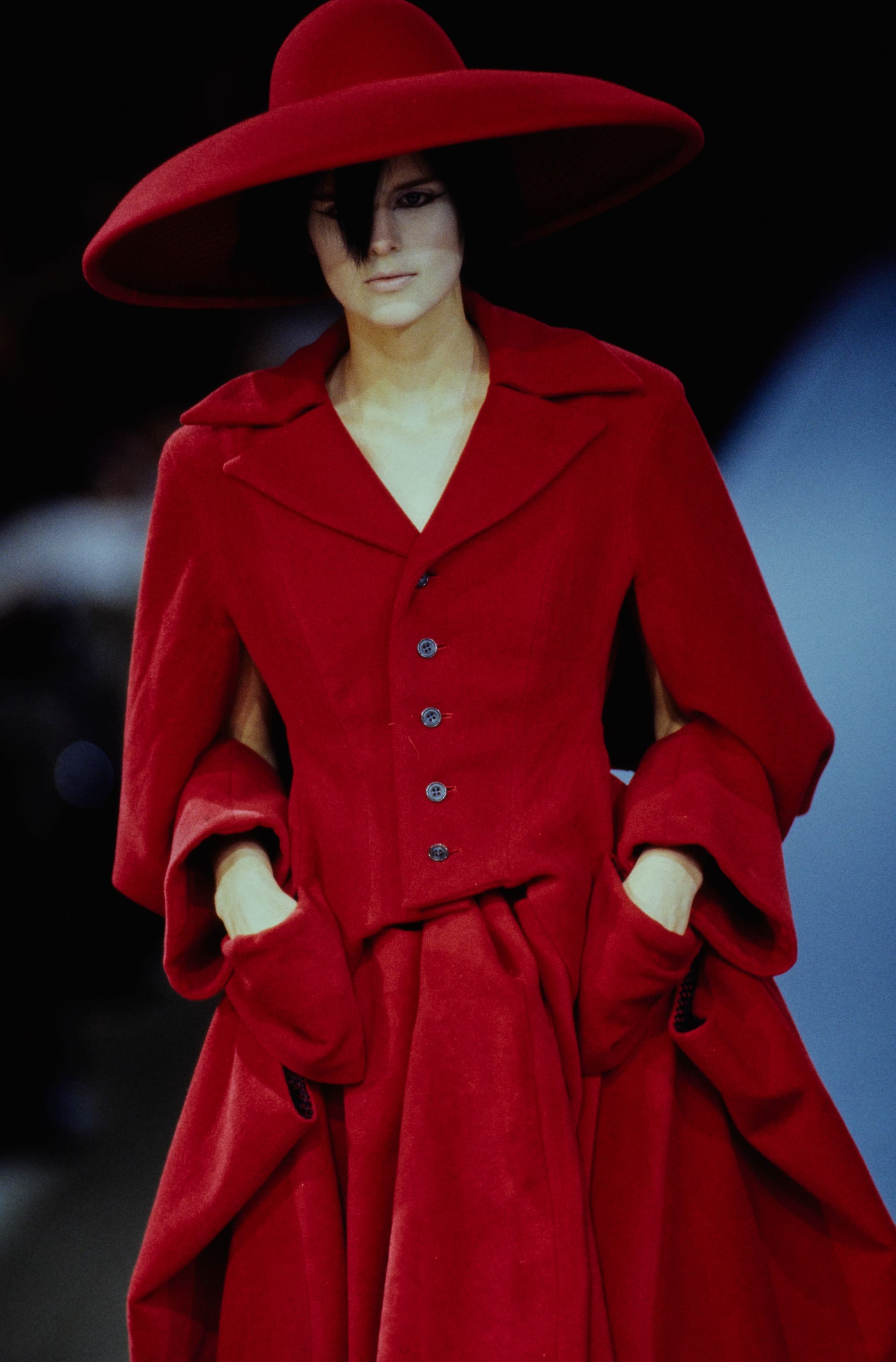 Yohji Yamamoto Fall 1995 detail 75: Wide-brimmed red hat and matching red jacket with oversized folded pocket shapes.