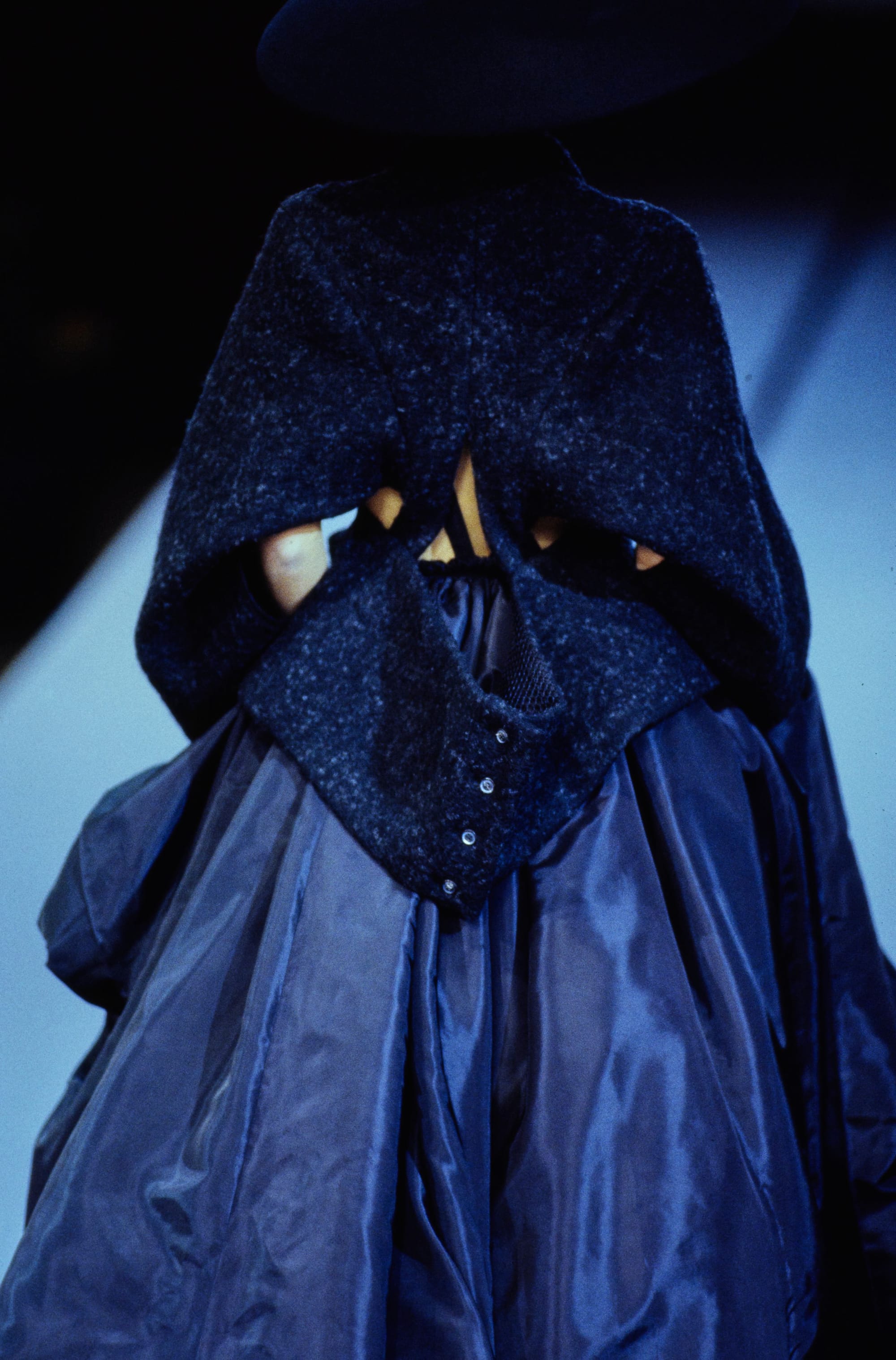 Yohji Yamamoto Fall 1995 detail 76: Rear navy cape with an opening at the waist above a glossy blue gathered skirt.