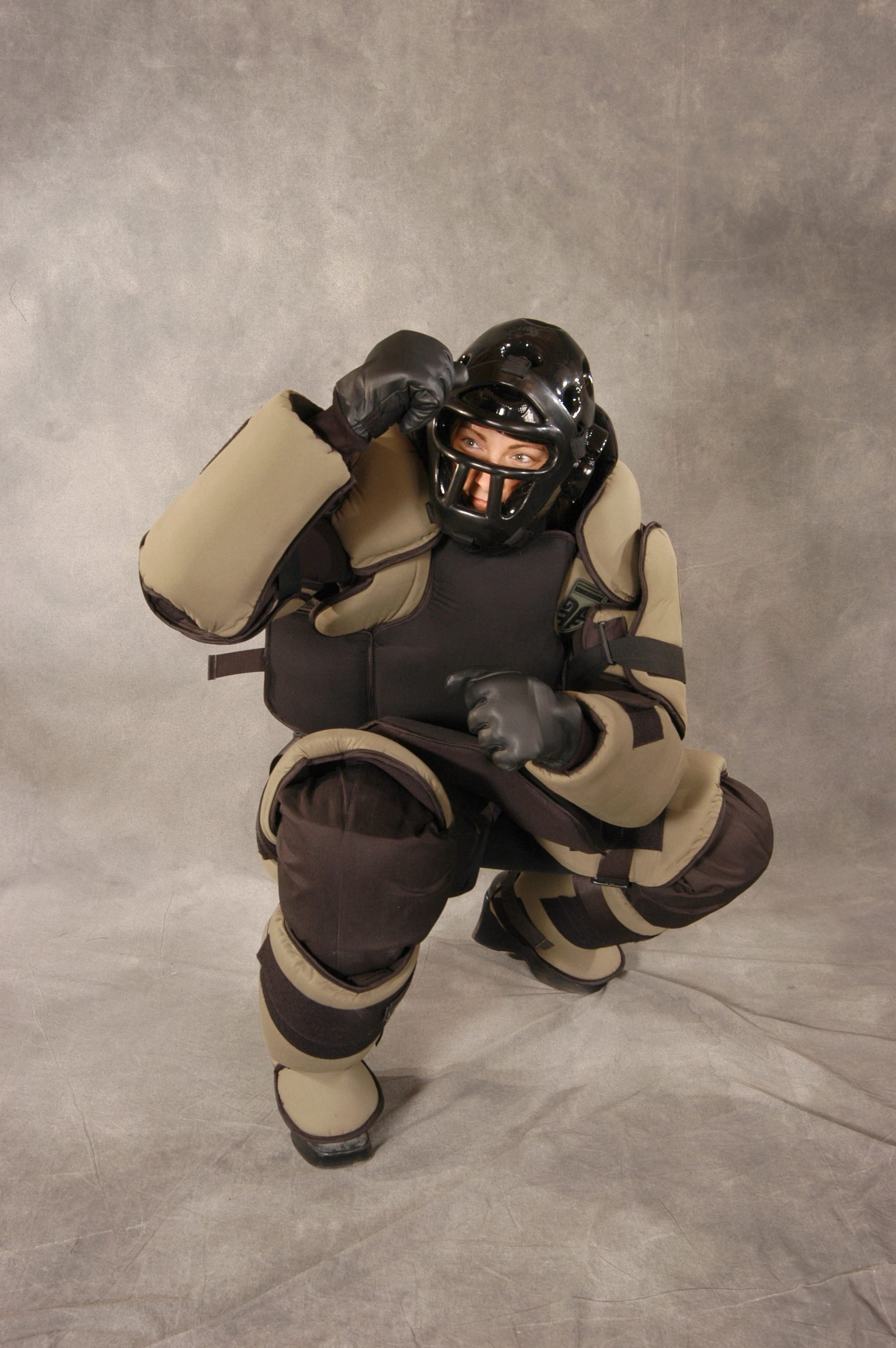 Khaki and black Mawashi T-RED training suit in a crouched defensive stance with helmet and gloves.
