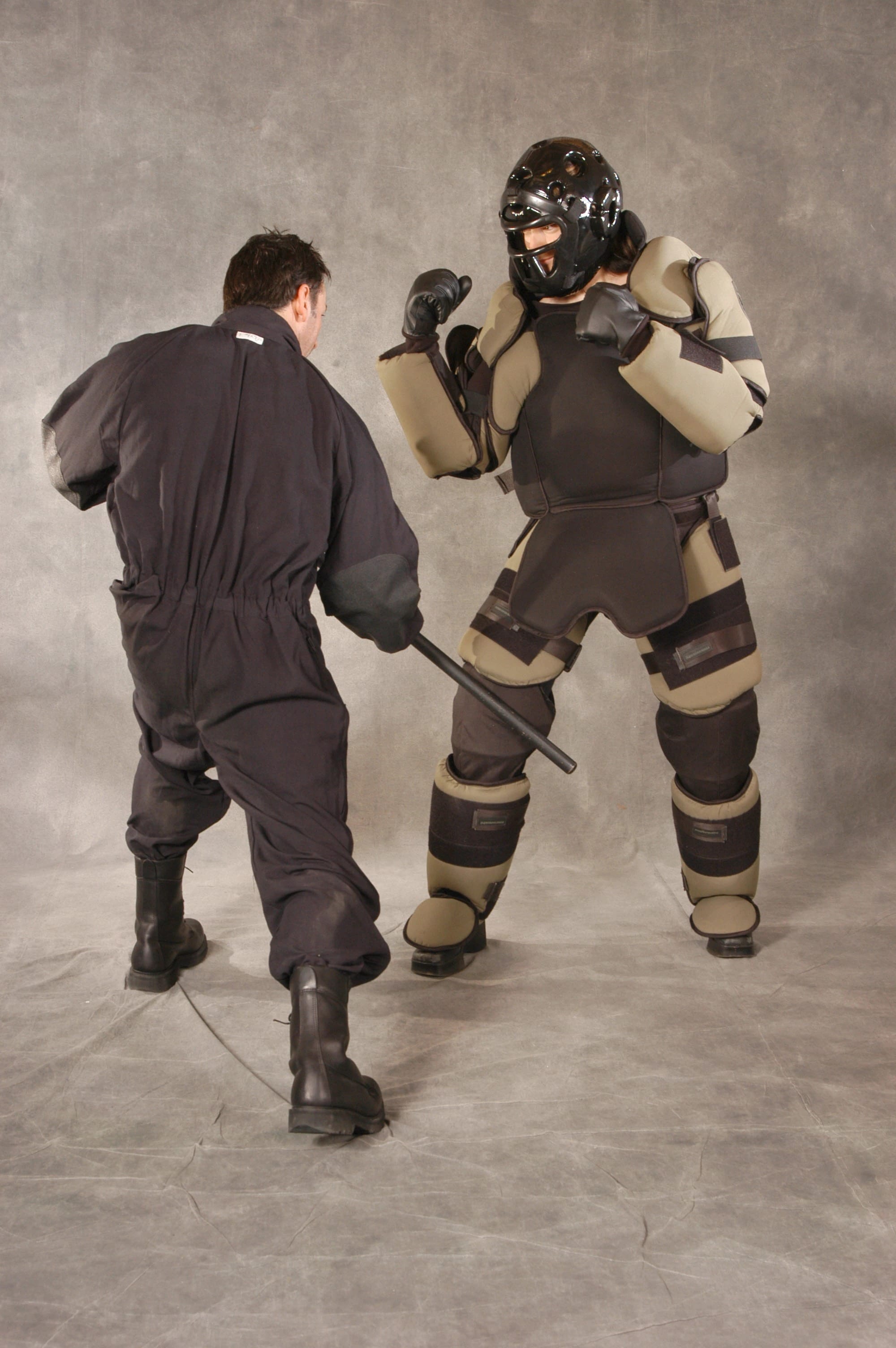Mawashi T-RED training suit during baton-strike practice, showing the full protective system in use.