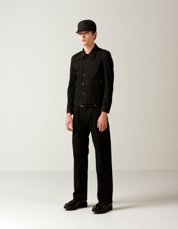 Male model in an all-black Man of Moods button-front jacket, wide trousers, and black cap.