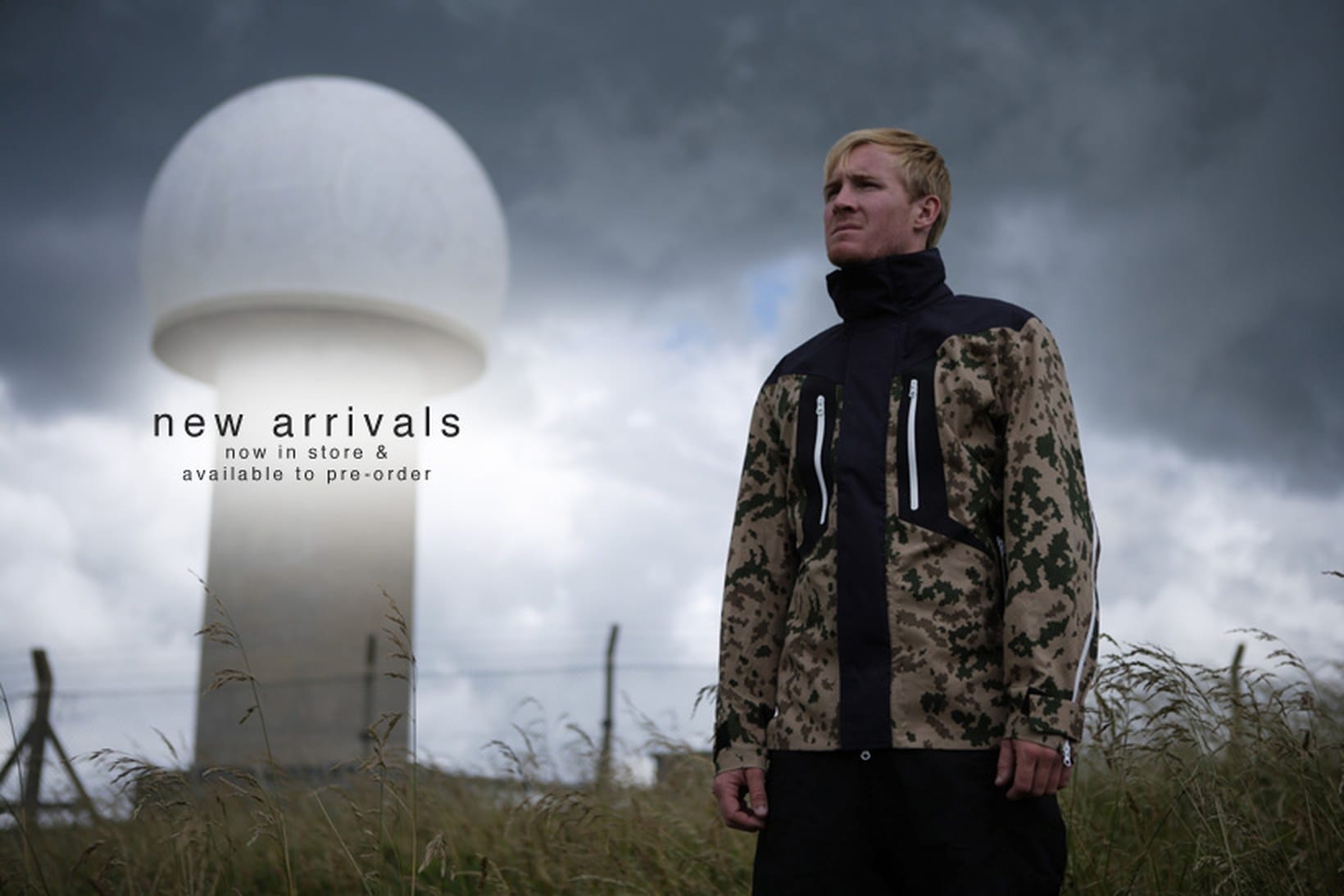 Model wearing the Griffin GFT 014 Technical Bearskin jacket in Finnish digital camouflage and black beside a white radar dome.