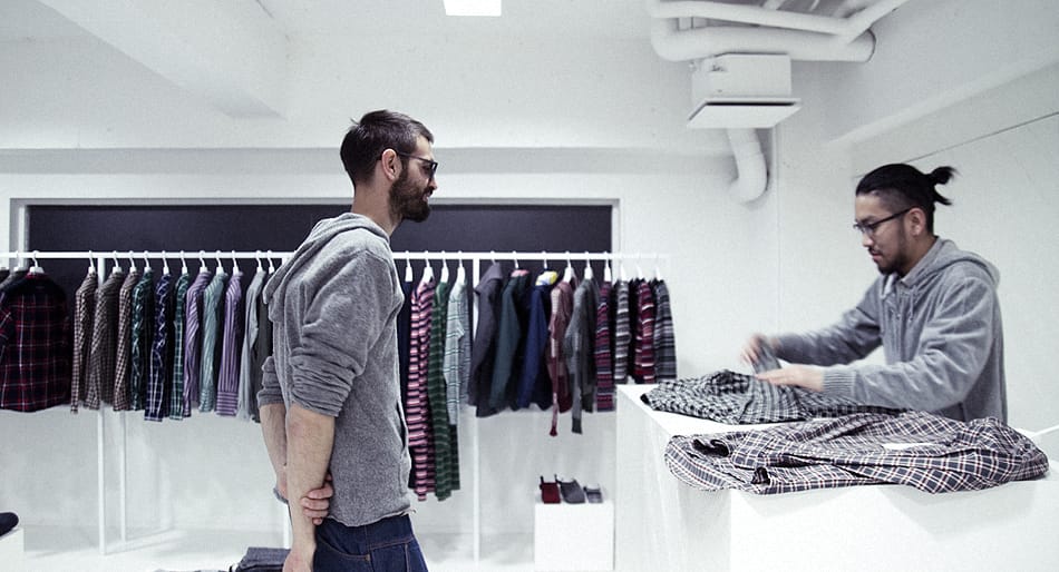 Yosuke Aizawa showing plaid White Mountaineering shirts to a visitor in the Tokyo showroom.