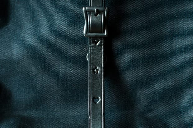 Black leather front buckle strap with shaped adjustment holes on the canvas rucksack.