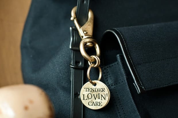 Brass clip and round keyring reading Tender Lovin Care beside the front pocket.