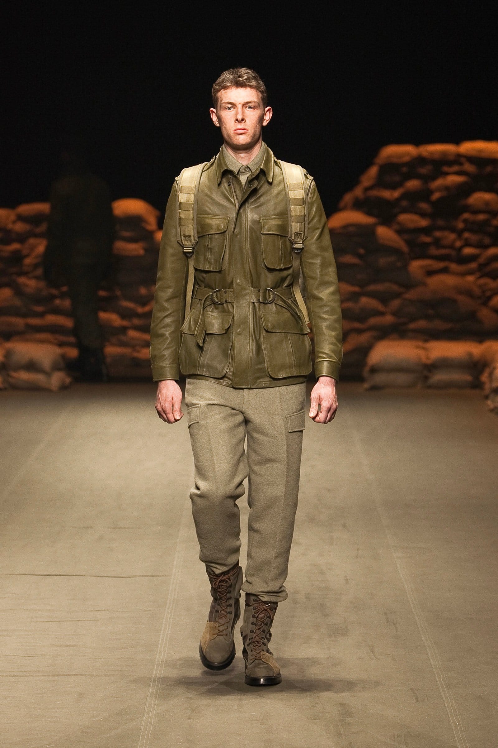 N.Hoolywood Autumn/Winter 2010–11 runway look 6: olive multi-pocket leather jacket with pale trousers and brown combat boots.