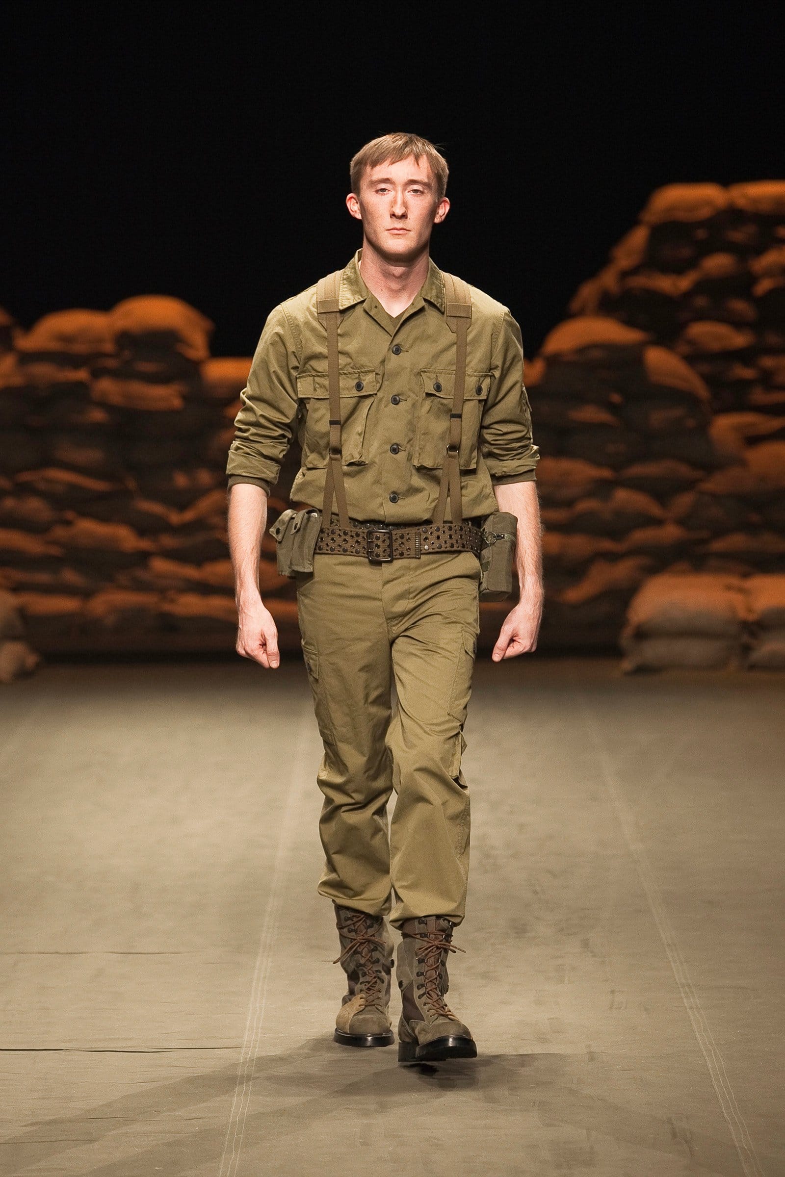 N.Hoolywood Autumn/Winter 2010–11 runway look 8: khaki field shirt and cargo trousers with belt, gloves, and brown combat boots.