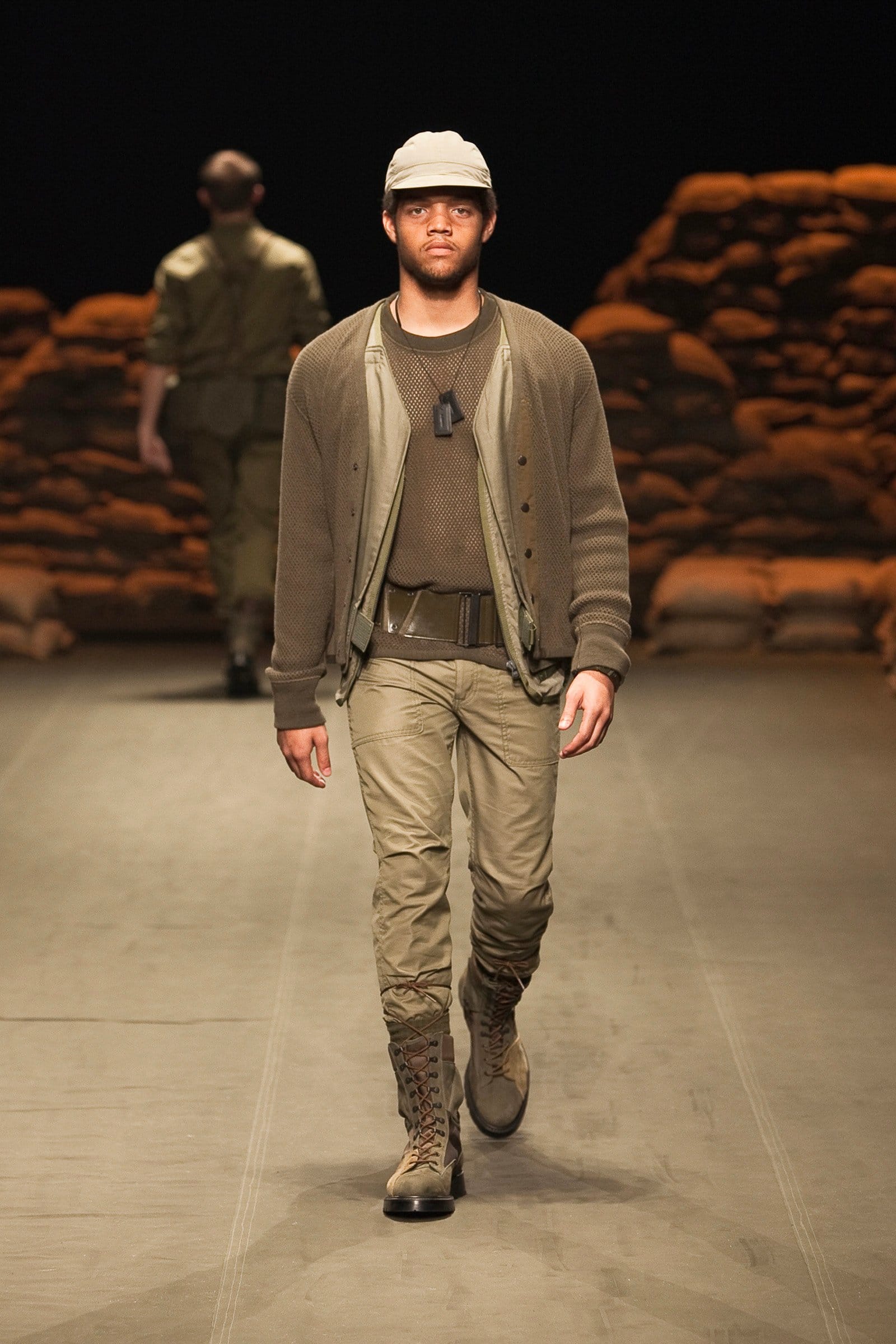 N.Hoolywood Autumn/Winter 2010–11 runway look 9: brown cardigan and layered shirt with khaki trousers, knit cap, and boots.