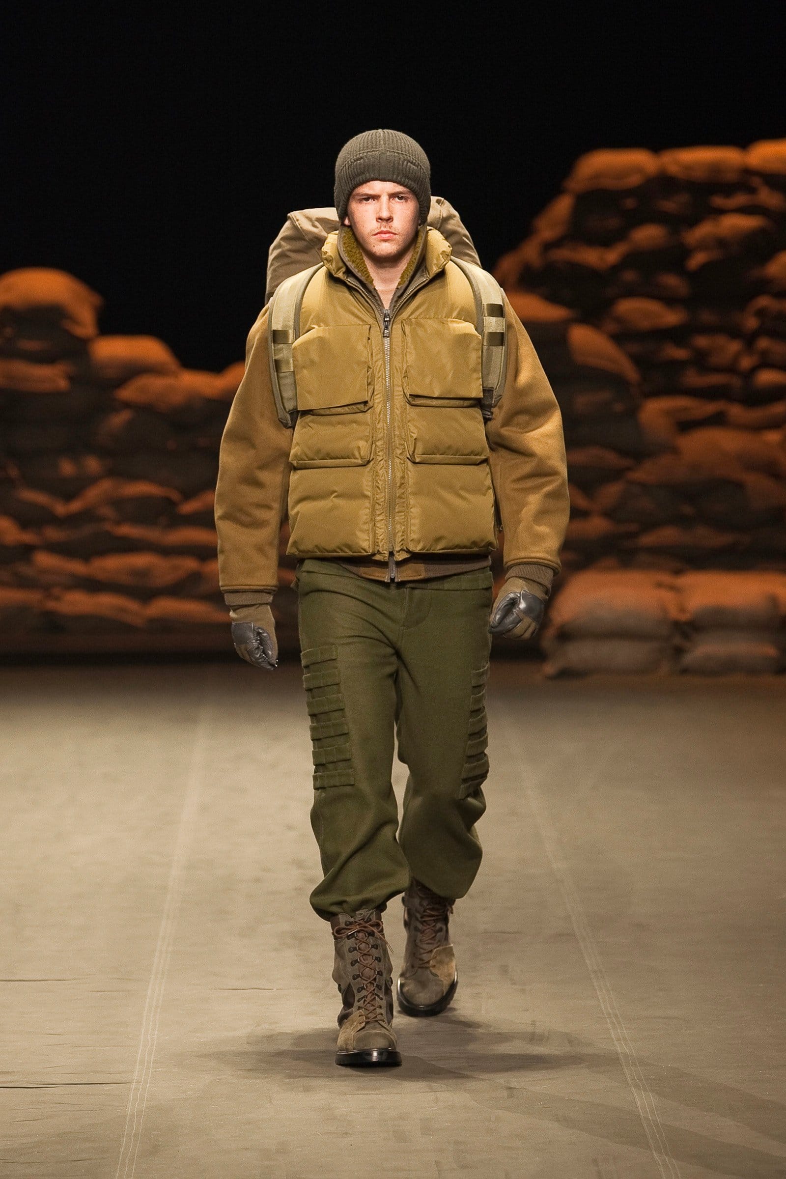 N.Hoolywood Autumn/Winter 2010–11 runway look 11: brown padded military jacket with olive trousers, knit cap, gloves, and boots.