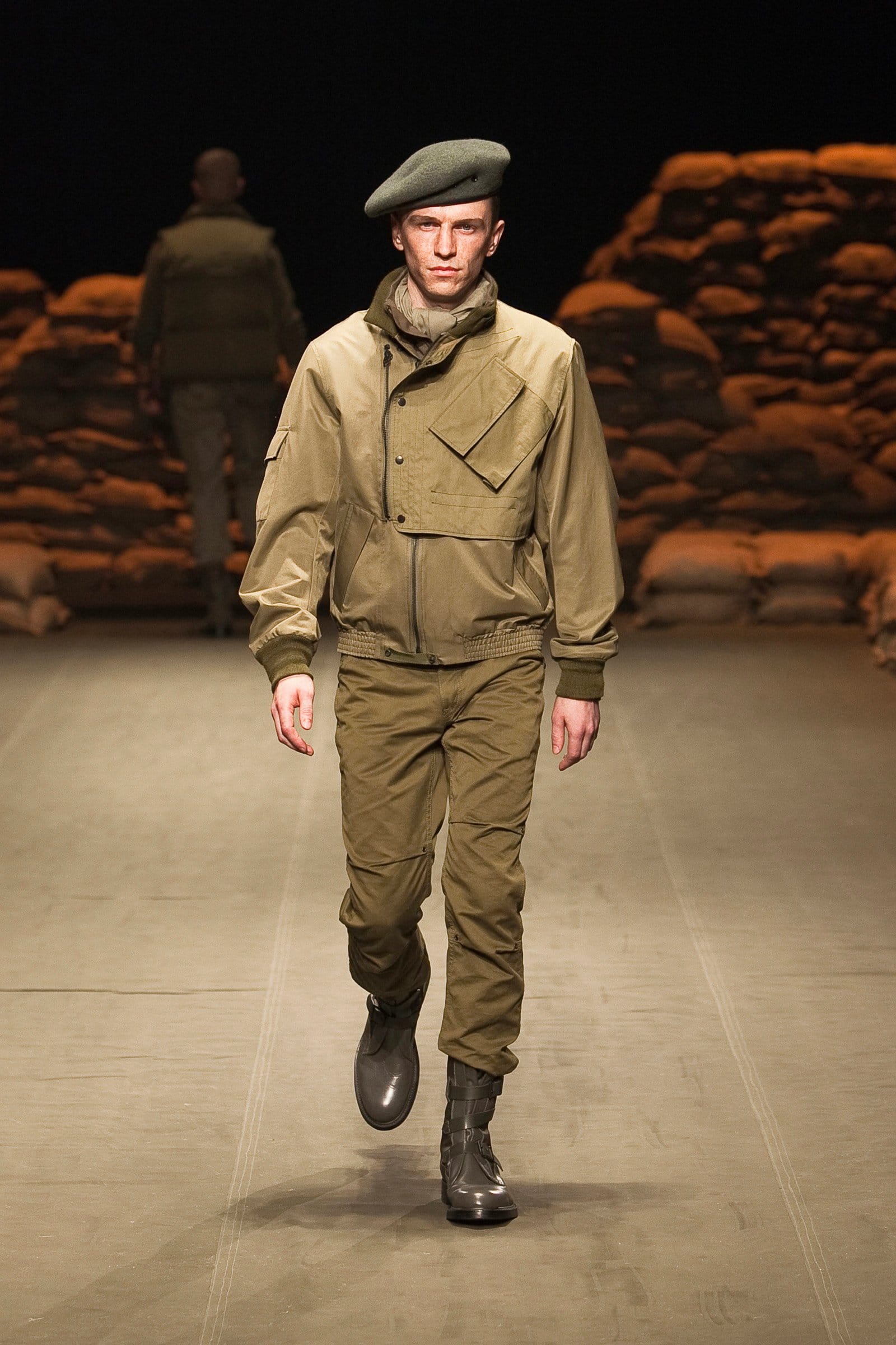 N.Hoolywood Autumn/Winter 2010–11 runway look 14: khaki field jacket and cargo trousers with scarf, beret, and black boots.