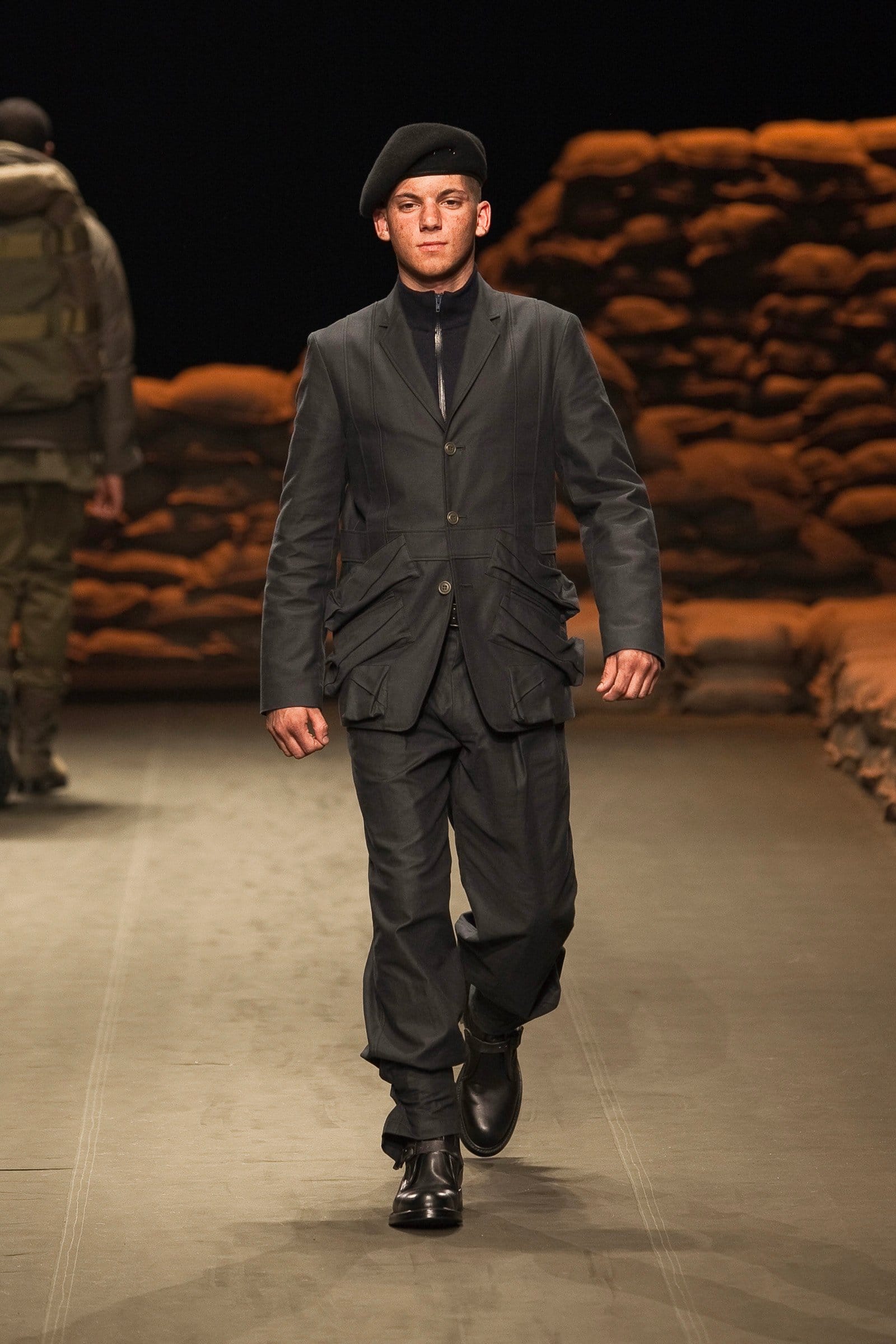 N.Hoolywood Autumn/Winter 2010–11 runway look 16: black tailored field jacket and trousers with black beret and boots.