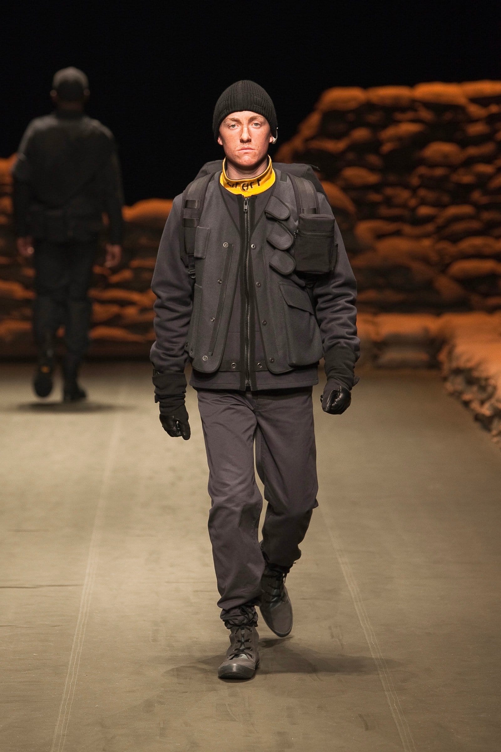 N.Hoolywood Autumn/Winter 2010–11 runway look 18: black layered military jacket with grey cargo trousers, gloves, and knit cap.