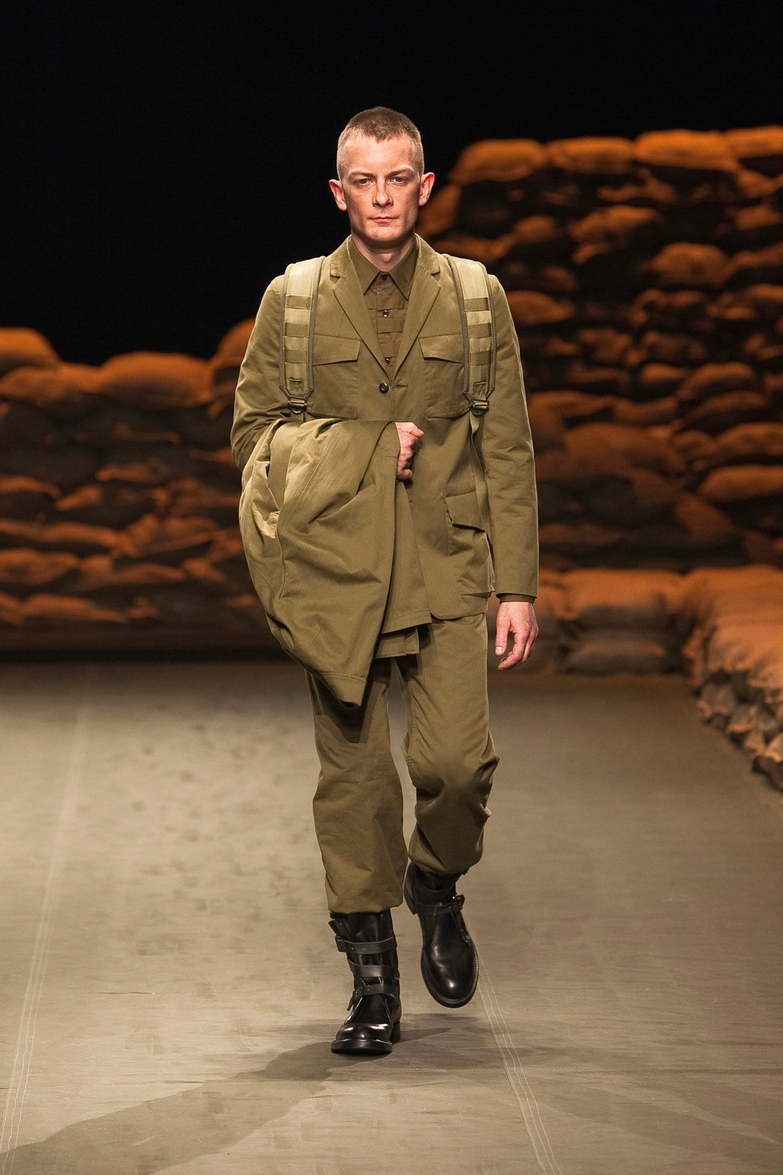 N.Hoolywood Autumn/Winter 2010–11 runway look 21: khaki long jacket carried over one shoulder with layered utility separates.