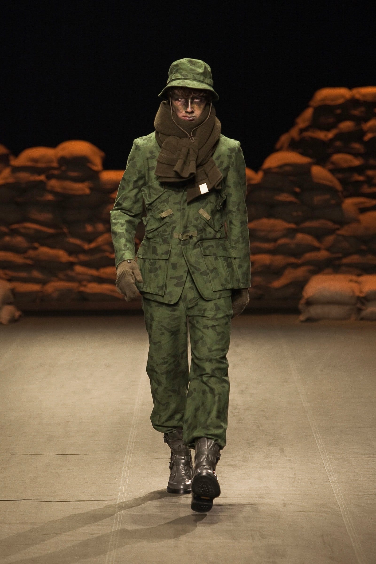 N.Hoolywood Autumn/Winter 2010–11 runway look 24: green camouflage hooded field jacket and trousers with face-covering scarf.
