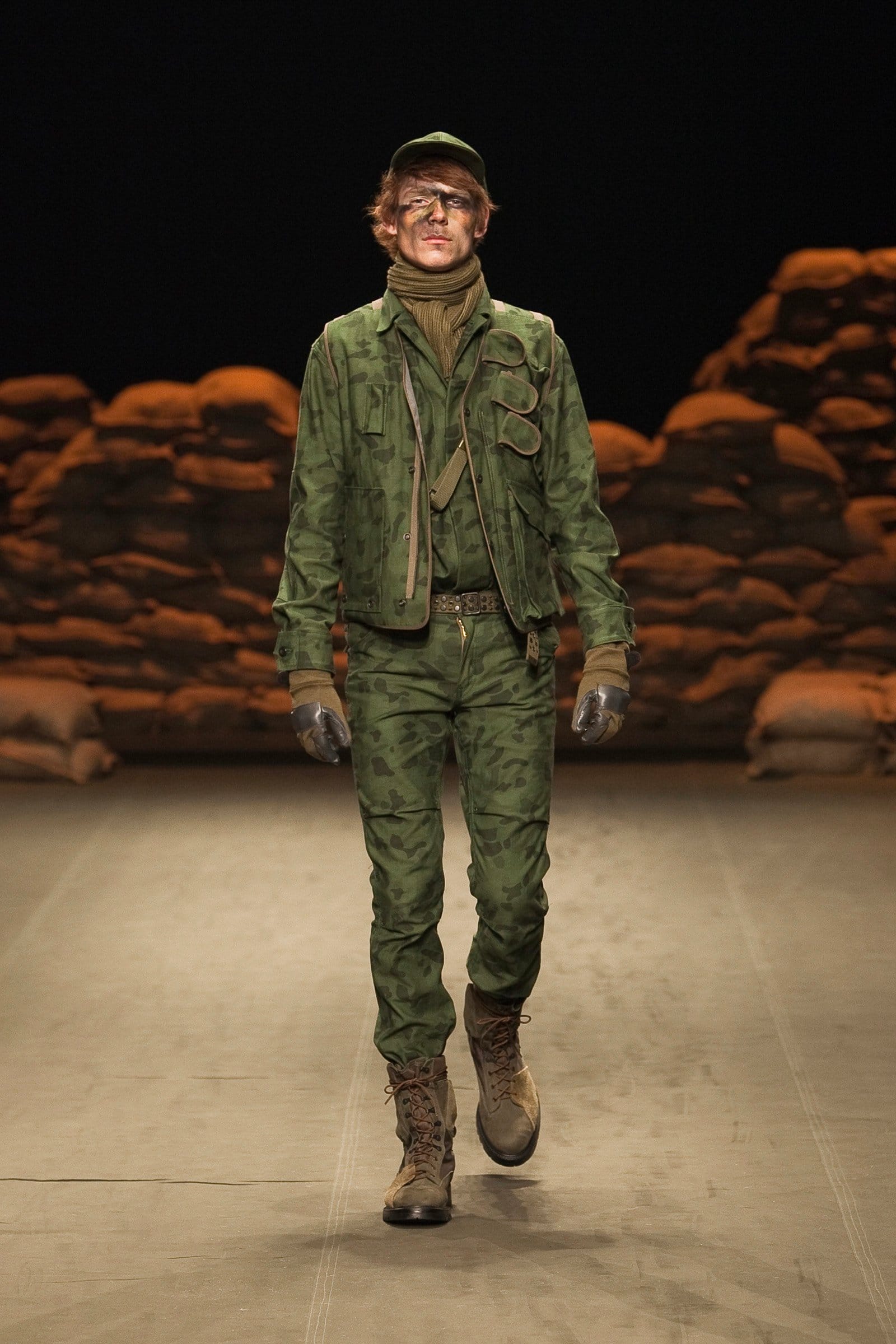 N.Hoolywood Autumn/Winter 2010–11 runway look 25: green camouflage field jacket and trousers with utility vest and gloves.