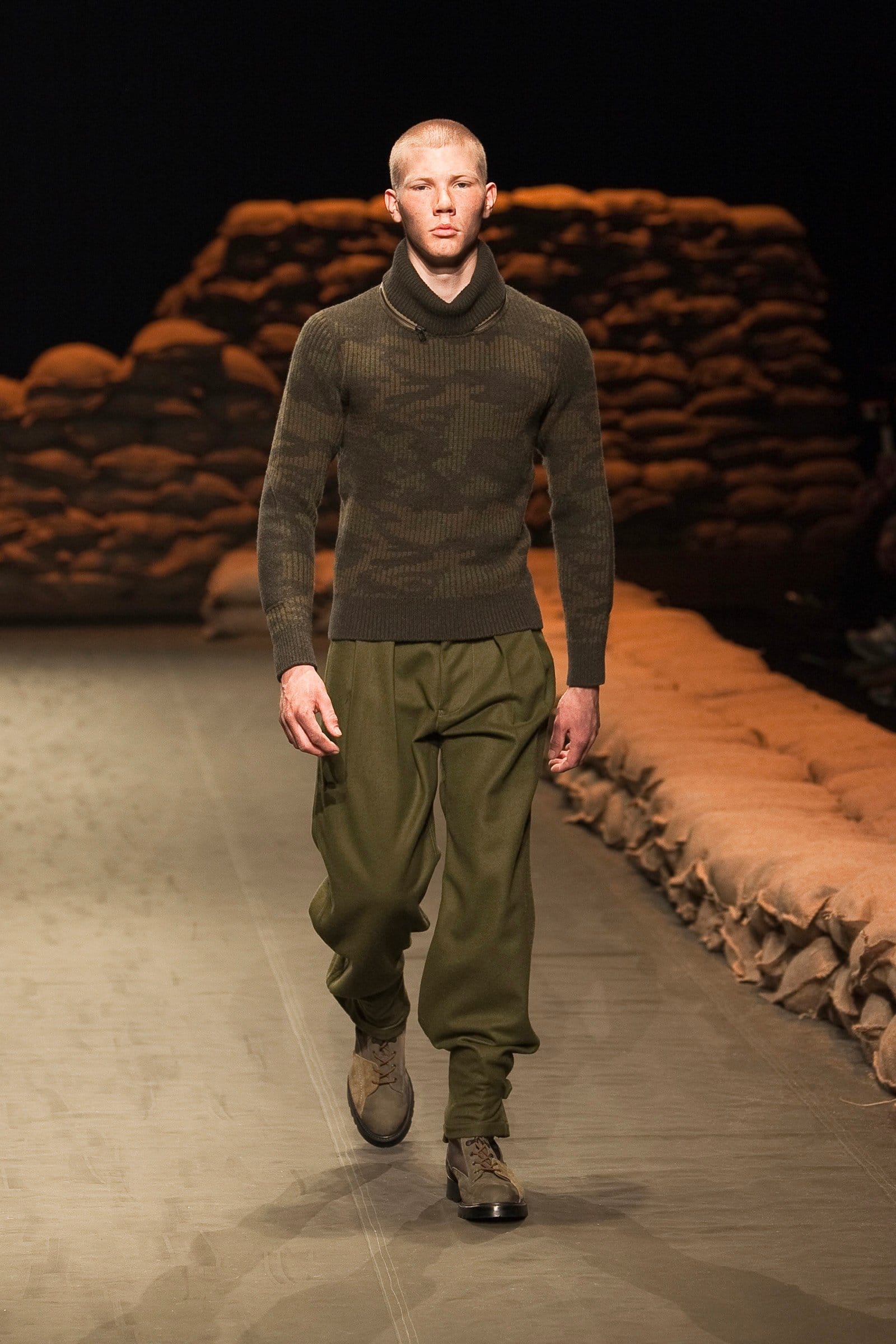 N.Hoolywood Autumn/Winter 2010–11 runway look 26: dark olive crewneck sweater with loose trousers and two-tone combat boots.