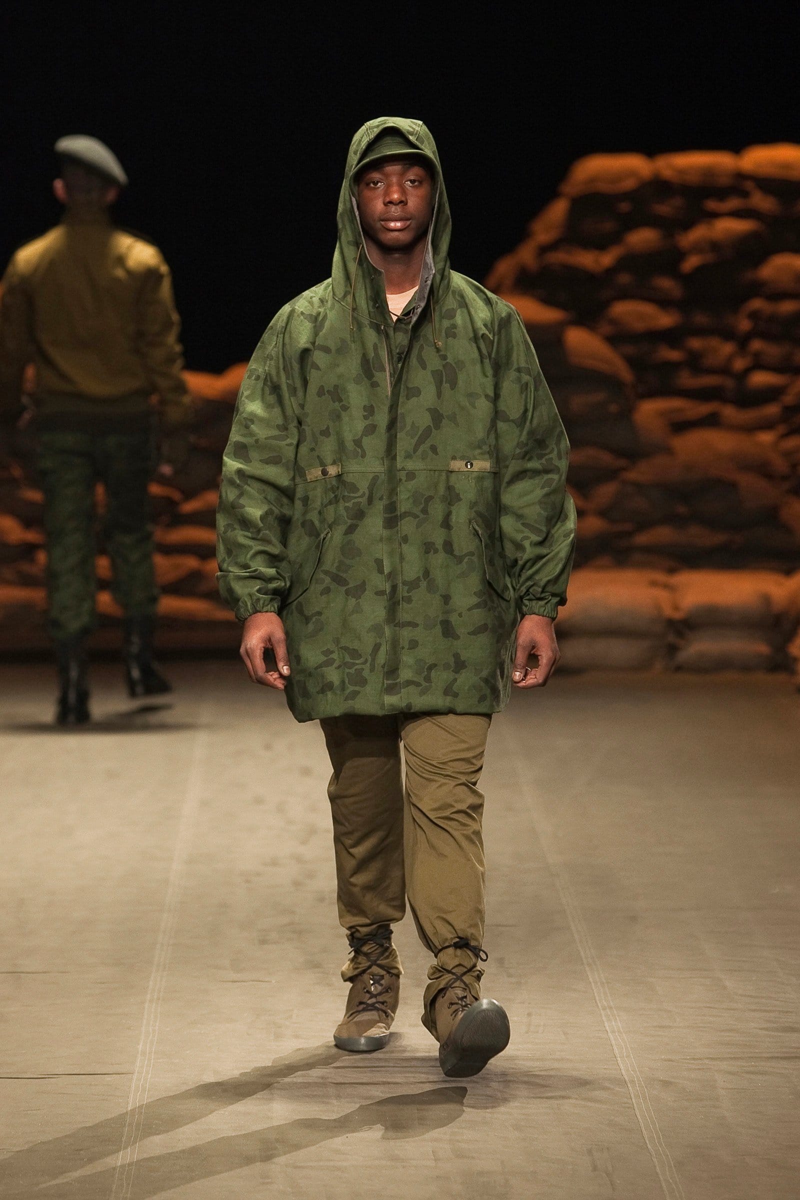 N.Hoolywood Autumn/Winter 2010–11 runway look 29: green camouflage hooded parka over khaki trousers and brown boots.