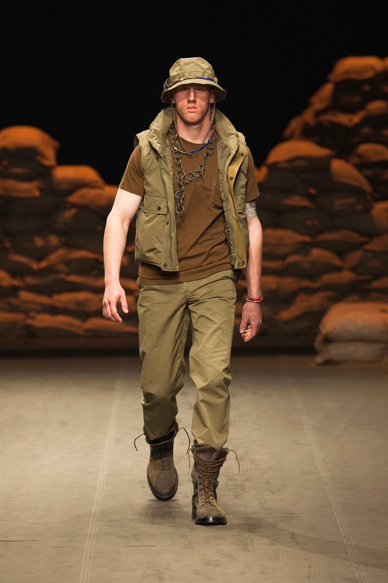 N.Hoolywood Autumn/Winter 2010–11 runway look 33: olive hooded vest over a brown T-shirt and khaki cargo trousers.