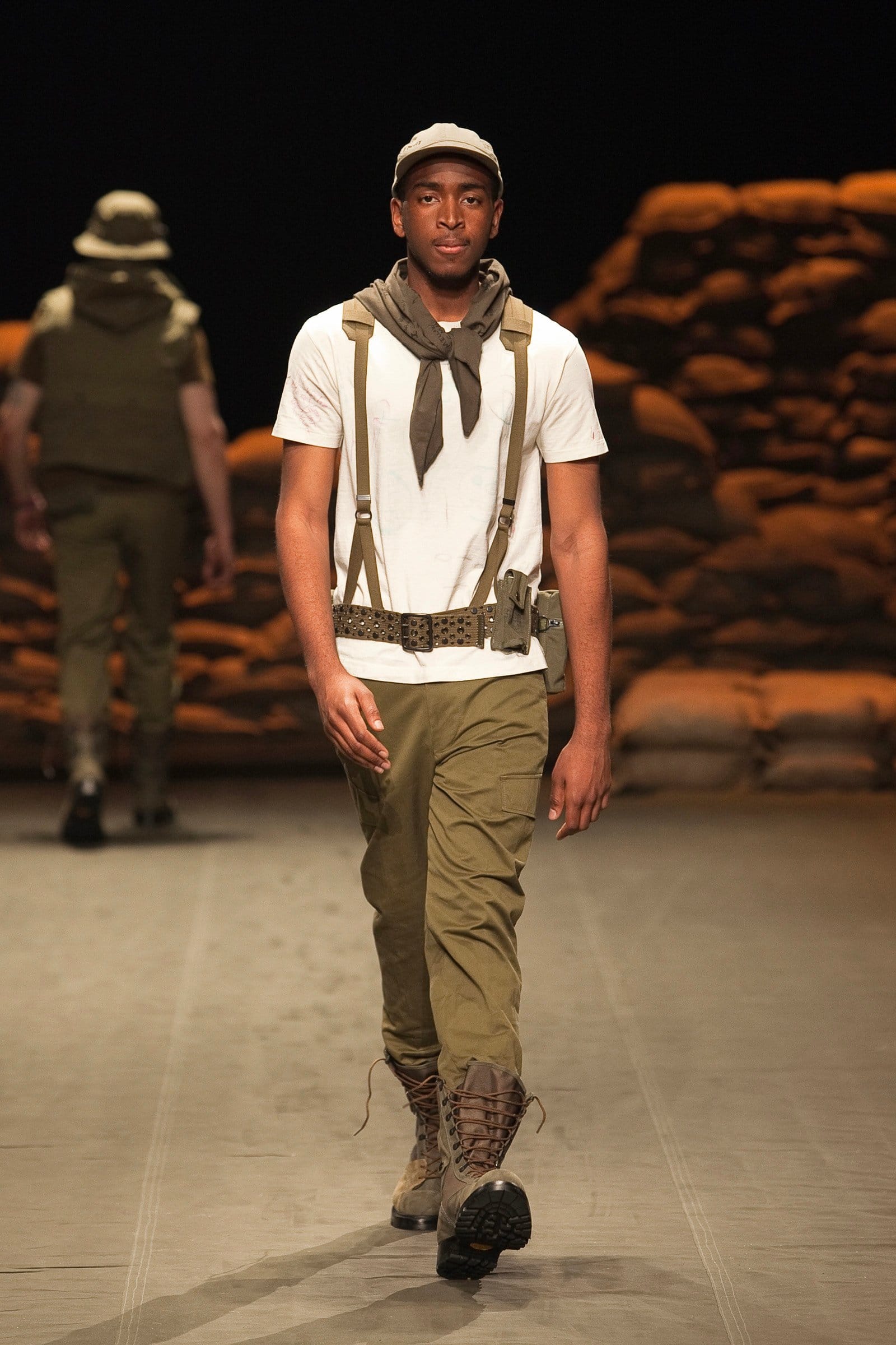 N.Hoolywood Autumn/Winter 2010–11 runway look 34: white T-shirt with khaki trousers, suspenders, scarf, cap, and combat boots.