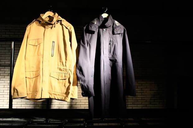 Tan Nike Sportswear NSW hooded jacket beside a dark trench coat on wooden hangers.