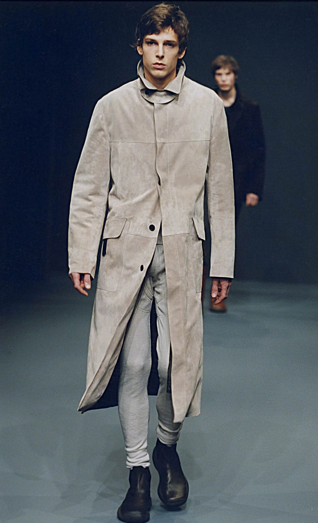 Prada Fall/Winter 1999 menswear runway look 1: light grey long coat over slim pale trousers and black boots.