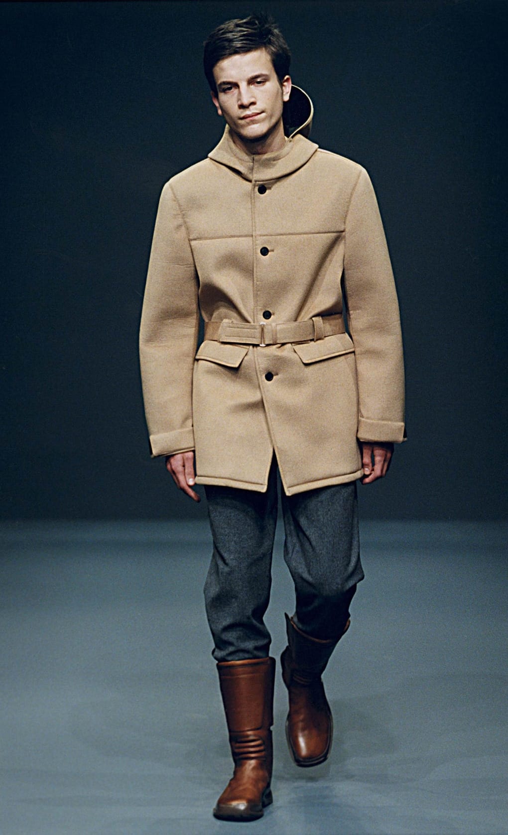 Prada Fall/Winter 1999 menswear runway look 11: belted camel field jacket with grey cropped trousers and brown boots.
