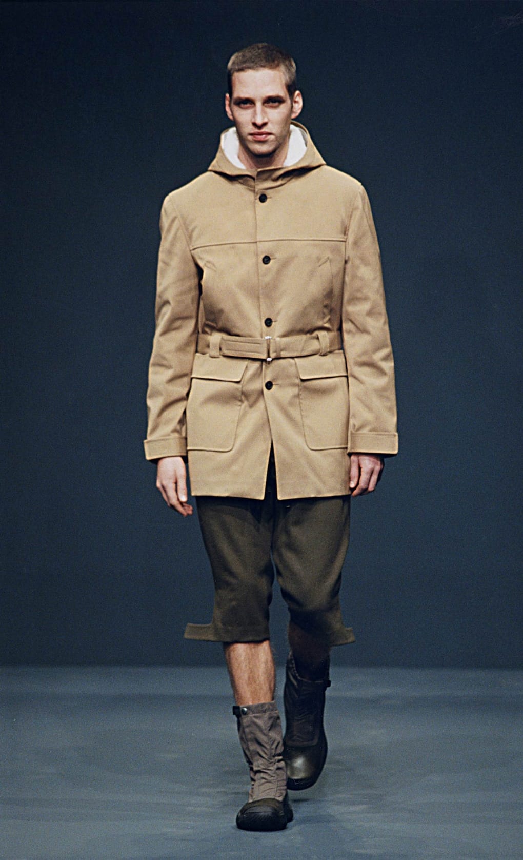 Prada Fall/Winter 1999 menswear runway look 16: tan hooded jacket with olive cropped trousers and grey boots.