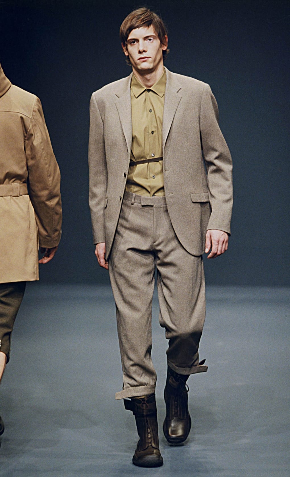 Prada Fall/Winter 1999 menswear runway look 17: grey suit layered over an olive shirt with black boots.