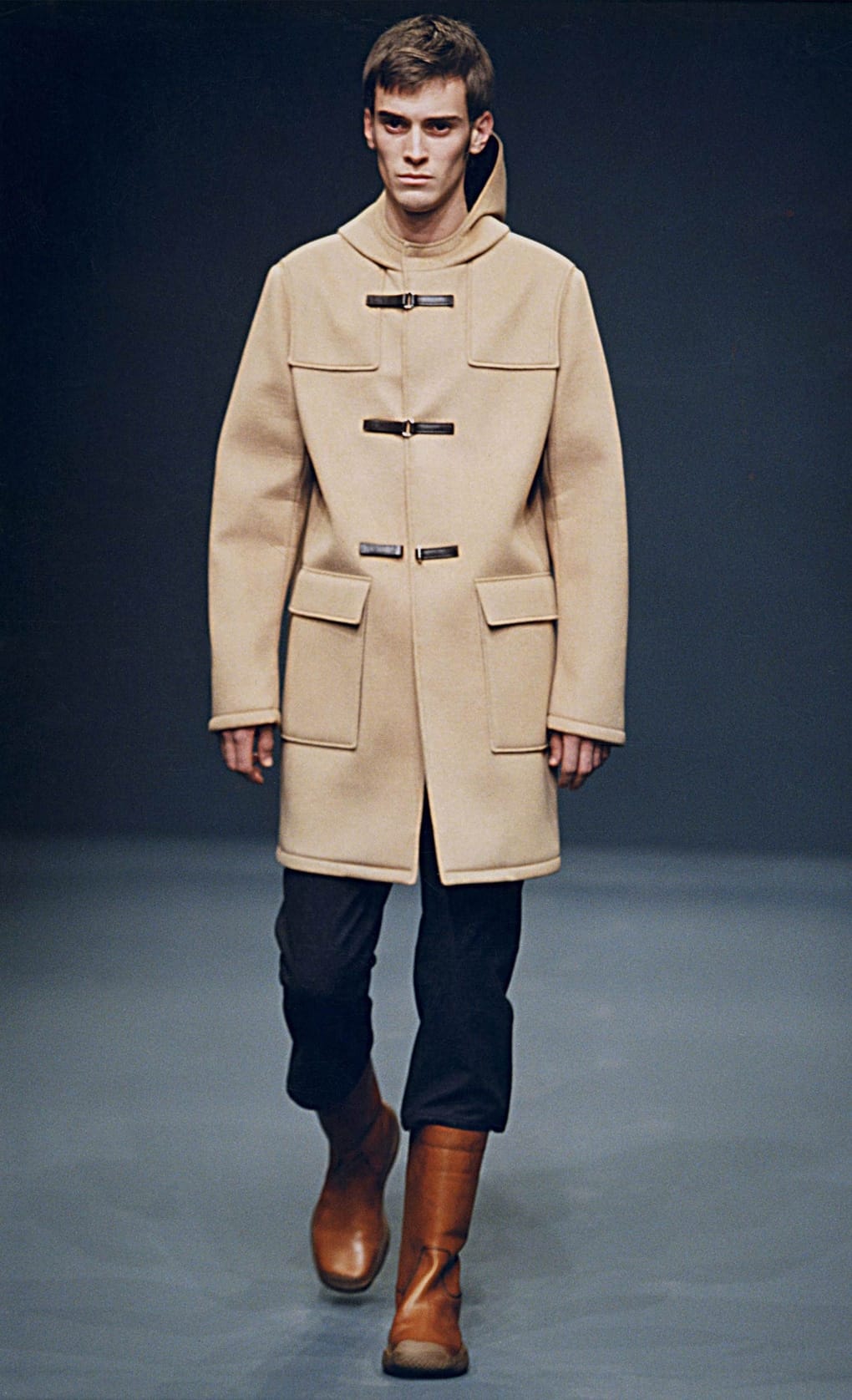 Prada Fall/Winter 1999 menswear runway look 19: camel duffle coat with dark cropped trousers and brown boots.