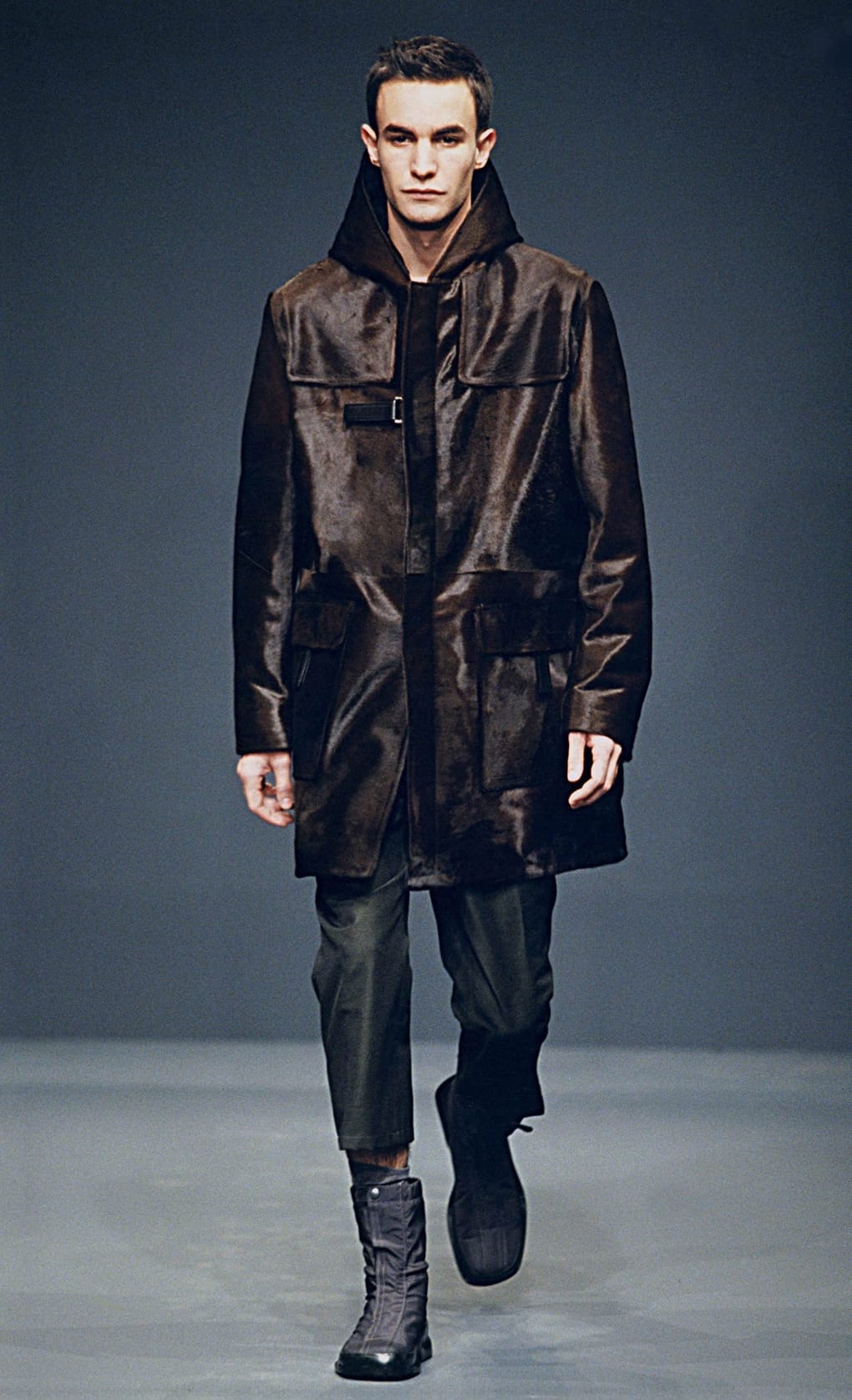 Prada Fall/Winter 1999 menswear runway look 21: dark brown hooded technical coat with cropped trousers and grey boots.