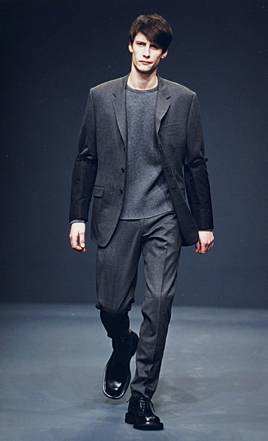 Prada Fall/Winter 1999 menswear runway look 27: charcoal blazer and cropped trousers layered over a grey top.