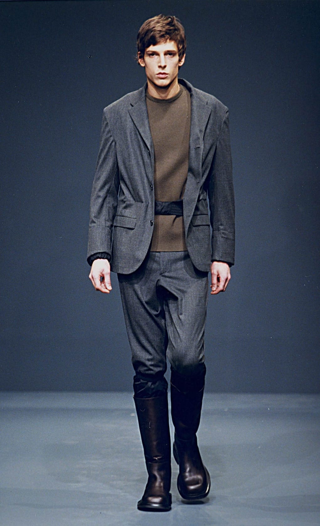 Prada Fall/Winter 1999 menswear runway look 30: grey layered blazer with belted cropped trousers and tall black boots.