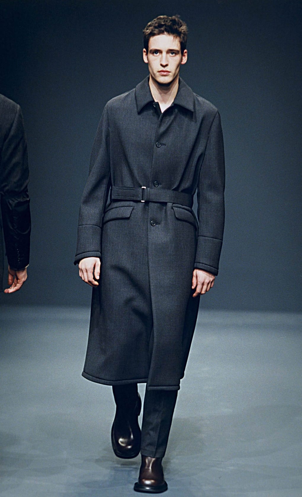 Prada Fall/Winter 1999 menswear runway look 35: dark belted coat with cropped trousers and black boots.