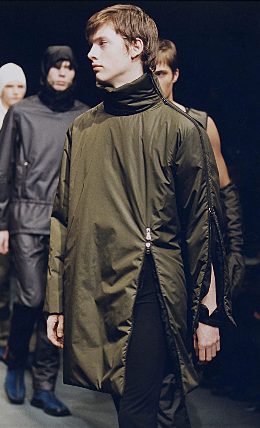 Prada Fall/Winter 1999 menswear runway look 42: olive sleeveless technical coat over black layers.