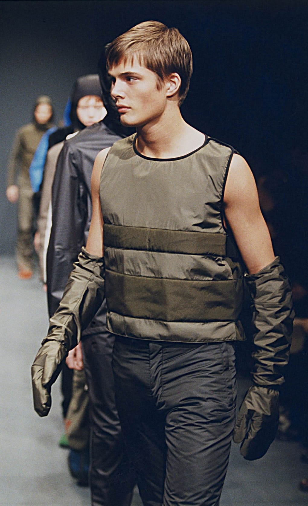 Prada Fall/Winter 1999 menswear runway look 43: olive padded sleeveless top with detached sleeves and dark trousers.