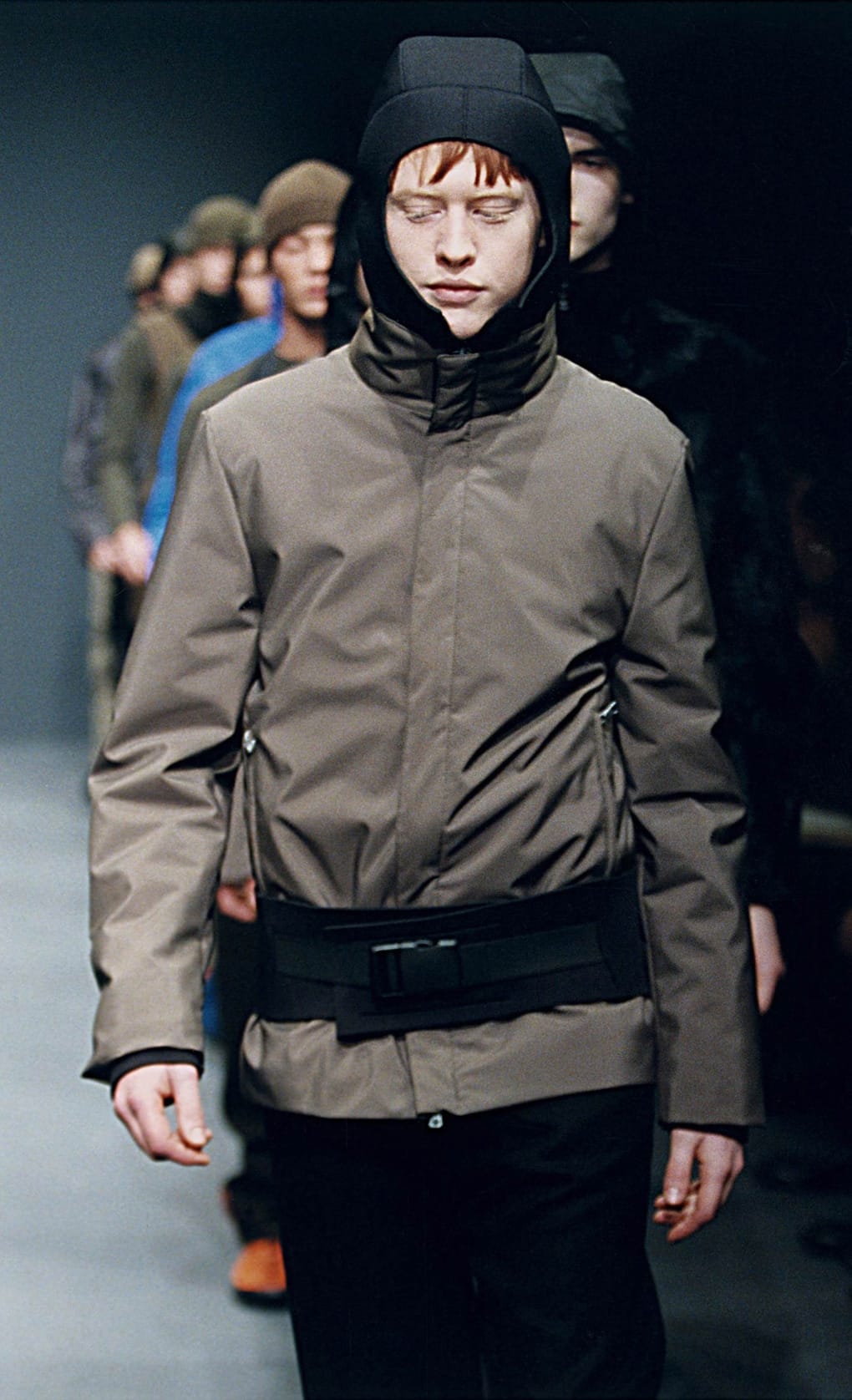 Prada Fall/Winter 1999 menswear runway look 46: taupe technical jacket with black hood and waist belt.