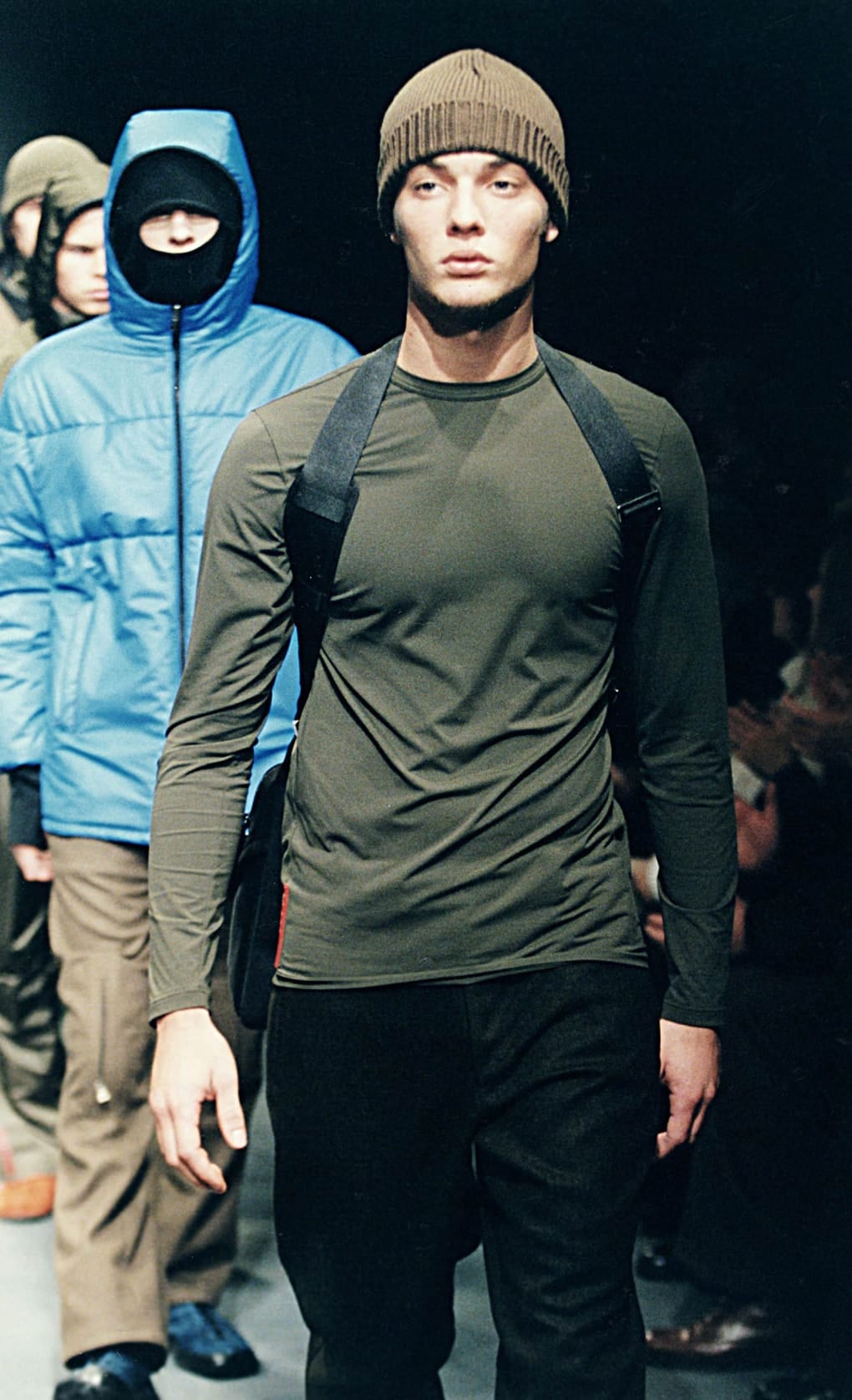 Prada Fall/Winter 1999 menswear runway look 49: olive performance top with black trousers, knit cap, and harness straps.