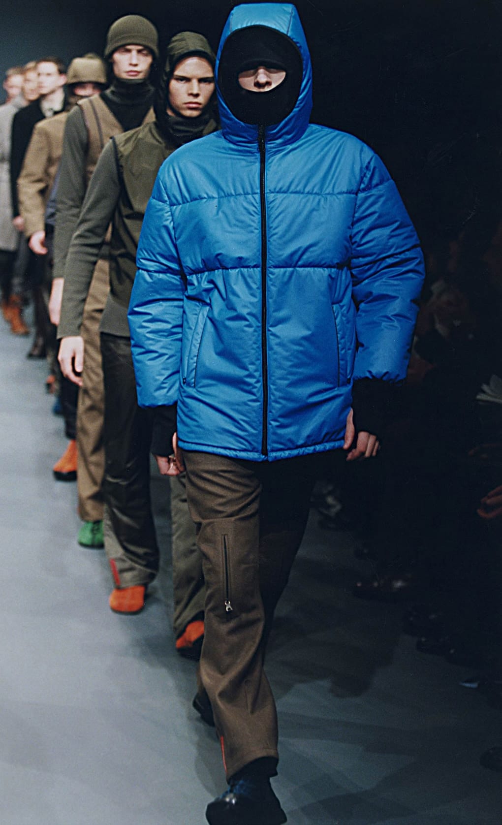 Prada Fall/Winter 1999 menswear runway look 50: bright blue padded jacket with brown trousers and black hood.