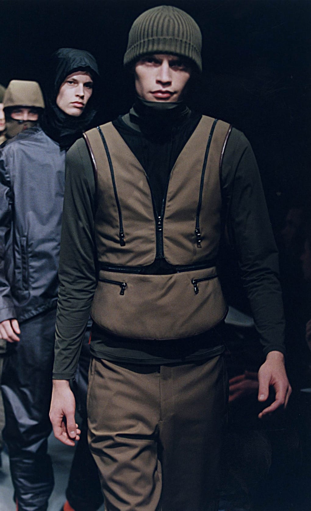Prada Fall/Winter 1999 menswear runway look 52: brown technical bib vest over a dark knit with matching trousers.