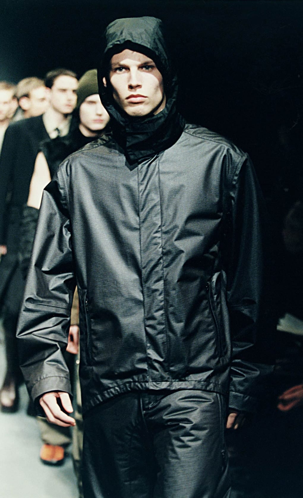 Prada Fall/Winter 1999 menswear runway look 53: black hooded zip jacket with glossy technical trousers.