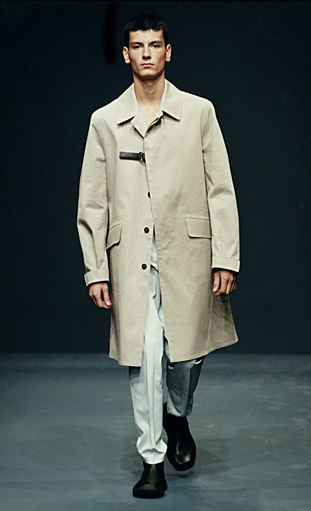 Prada Fall/Winter 1999 menswear runway look 58: pale taupe long coat with light trousers and black boots.
