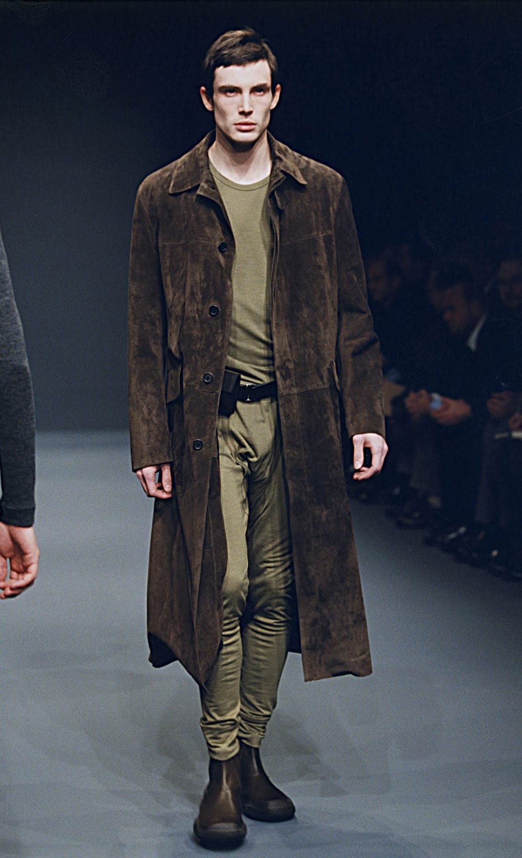 Prada Fall/Winter 1999 menswear runway look 6: dark brown long coat over an olive top and trousers.