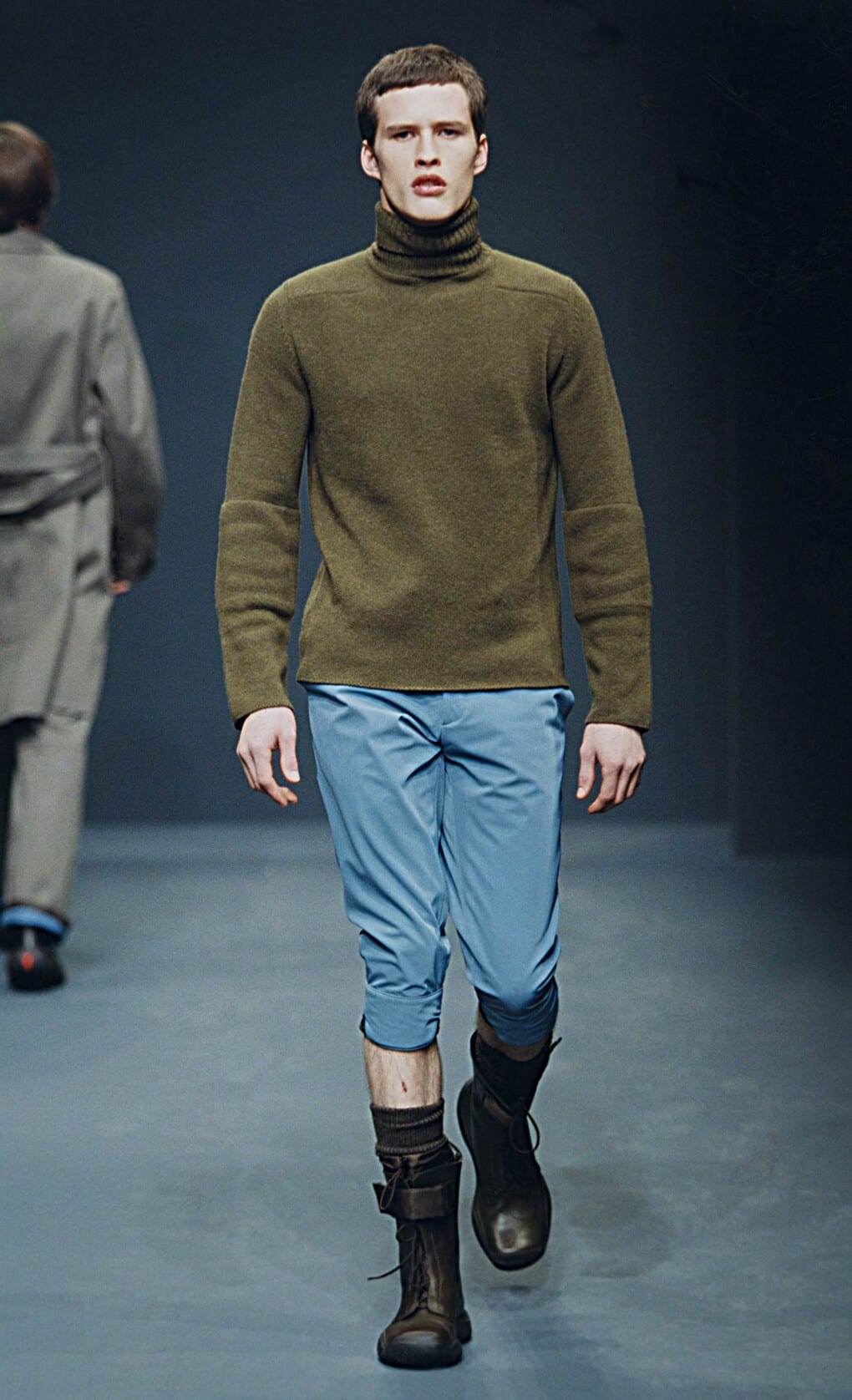 Prada Fall/Winter 1999 menswear runway look 61: olive turtleneck with pale blue cropped trousers and brown boots.
