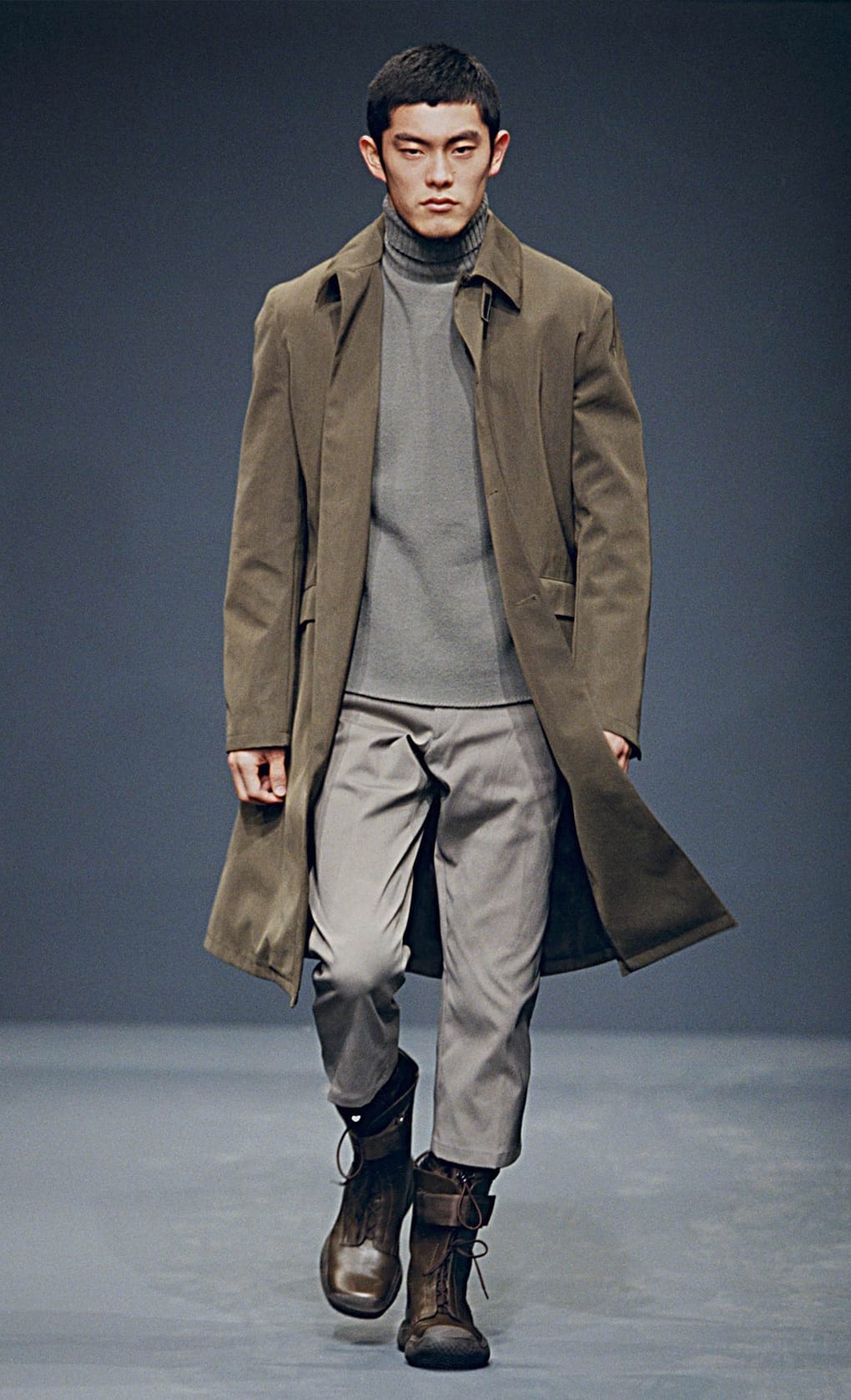 Prada Fall/Winter 1999 menswear runway look 63: brown long coat over a grey turtleneck with cropped trousers.