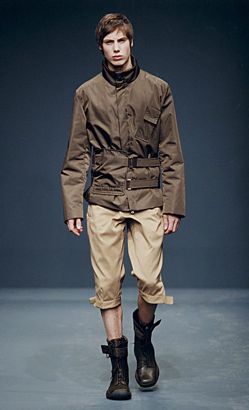 Prada Fall/Winter 1999 menswear runway look 64: brown belted jacket with tan cropped trousers and tall boots.
