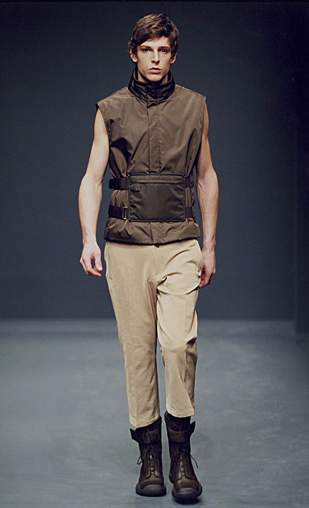 Prada Fall/Winter 1999 menswear runway look 66: brown sleeveless belted vest over a dark top with pale trousers.